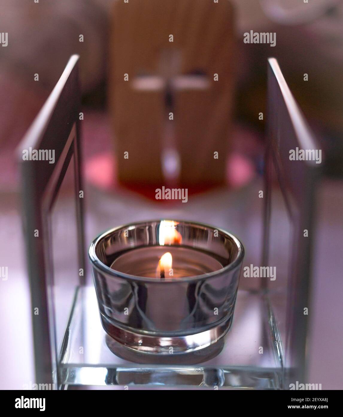 Eine Kerze, die vor einem Kreuz (Hintergrund, unscharf) platziert wird, um das vergangene Jahr 2020/21 zu reflektieren. Coronavirus. Tag der Reflexion Stockfoto