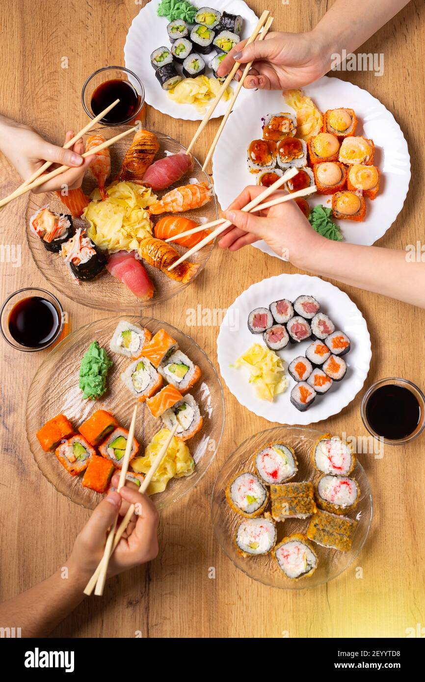 Perfektes Familienessen mit einer reichhaltigen und abwechslungsreichen Auswahl an Sushi. Verschiedene Lachs, Krabben, vegane Brötchen, Wasabi, Ingwer auf Holzhintergrund. Japanisch Stockfoto