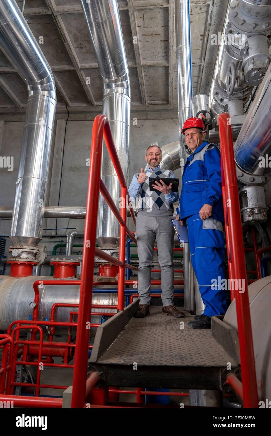 Ingenieur, der im industriellen Innenraum mit großen Rohrleitungen steht. Manager Gibt Daumen Hoch. Industrie 4,0 Stockfoto