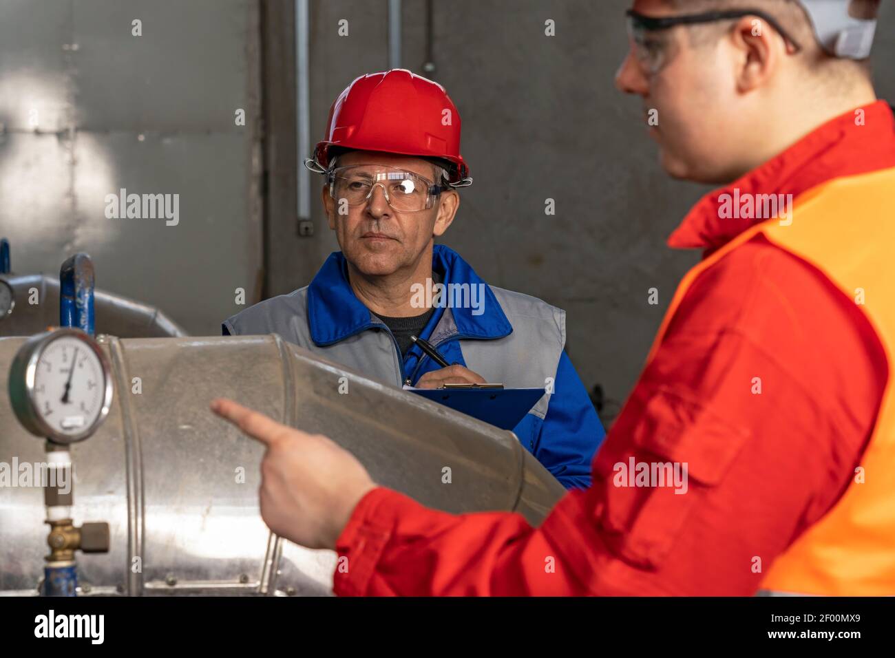 Zwei Arbeiter neben Manometer im Fernwärmekraftwerk. Teamwork-Konzept. Stockfoto
