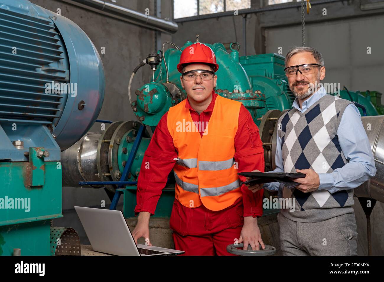 Junge Arbeiter mit Laptop-Computer für die Datenprüfung. Porträt des Managers und Arbeiters im Fernwärmekraftwerk. Teamwork-Konzept. Industrie 4,0 Stockfoto