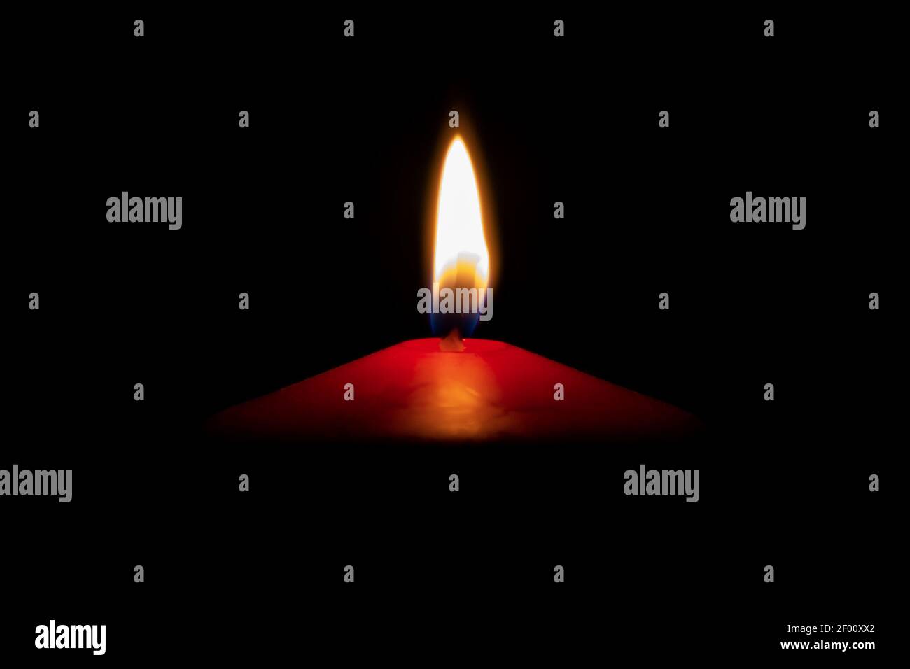Isolierte rote Kerze mit Flamme vor dunklem Hintergrund Stockfoto