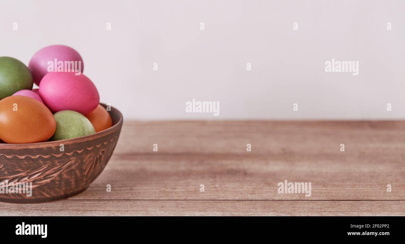 Bunte Hühnereier mit natürlichen Lebensmittelfarben in einem Tonteller auf einem Holztisch bemalt. Banner. Osterfeiertagskonzept Stockfoto
