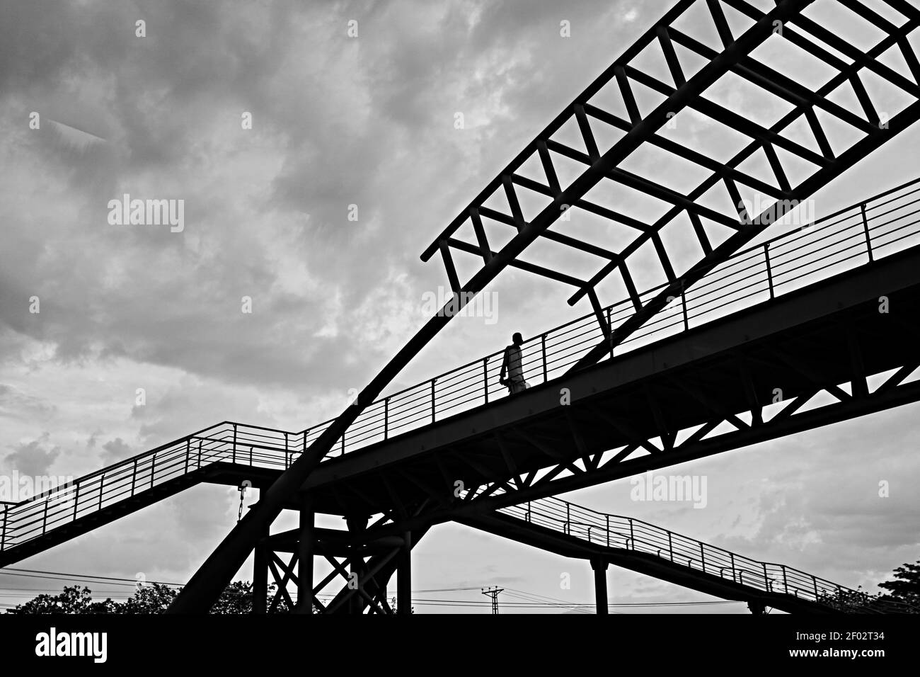 Eine Graustufenaufnahme eines Mannes, der durch das Bild geht Eine Brücke unter dem wolkigen Himmel Stockfoto