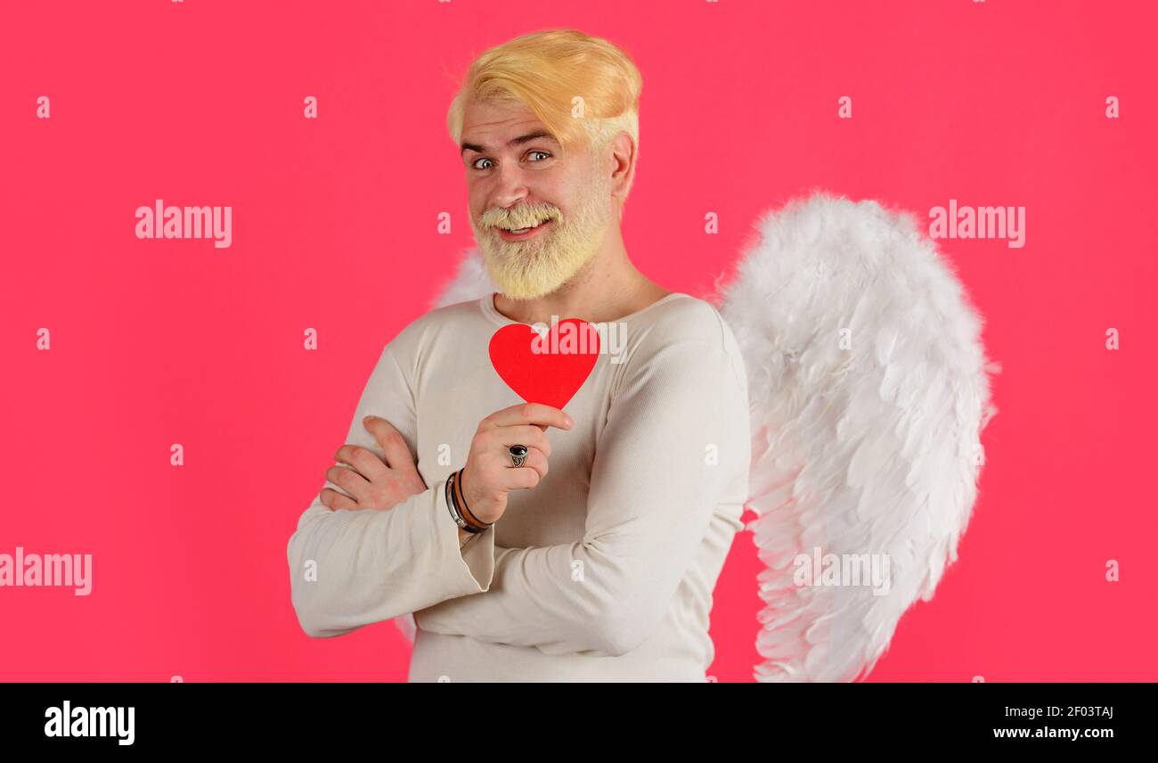 Liebeskonzept. Schöner Engel mit rotem Herzen. Bärtiger Mann mit Engelsflügeln. Valentinstag. Stockfoto