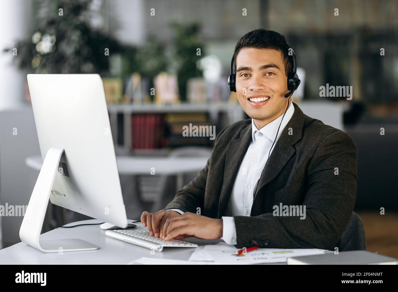 Porträt eines männlichen Mitarbeiters des Callcenters. Lächelnder hispanischer Mann schaut auf die Kamera, sitzt im modernen Büro mit Headset, führt Video-Meeting, Support-Service-Konzept Stockfoto