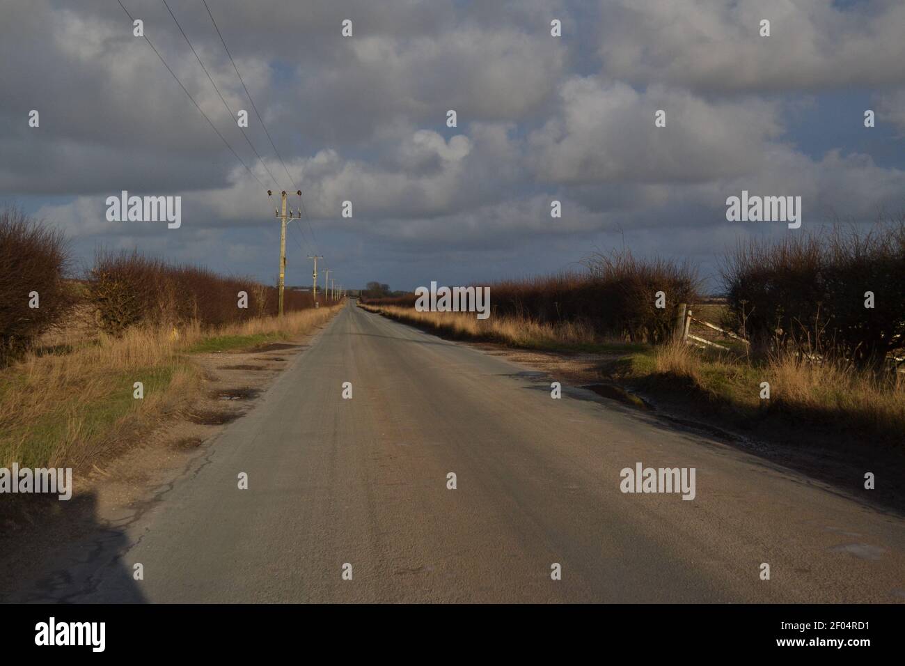 Land Tarmac Road an EINEM hellen sonnigen Tag - flauschig Wolken in EINEM blauen Himmel - Straße mit Hecken gesäumt - Country Lane ohne Straßenmarkierungen - Yorkshire UK Stockfoto