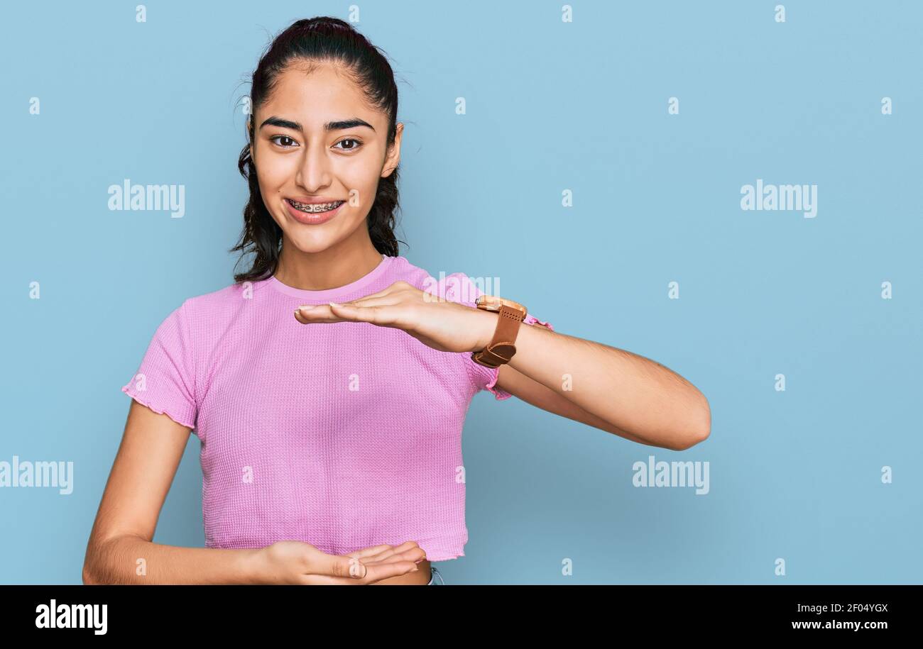 Hispanic Teenager Mädchen mit Zahnspangen tragen lässige Kleidung gesturing mit Händen zeigt große und große Größe Zeichen, Maßnahme Symbol. Lächelnd suchen Stockfoto