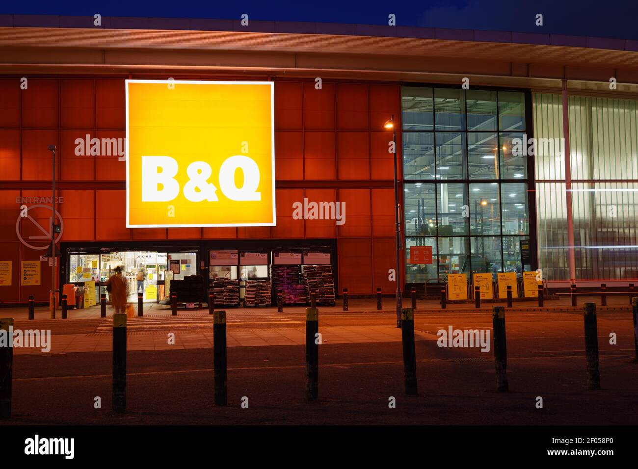 Der Eingang des B&Q-Stores wurde bei den abendlichen Einkaufsstunden in London beleuchtet, weiße Schriftzüge in orangefarbenem Hintergrundbanner Stockfoto