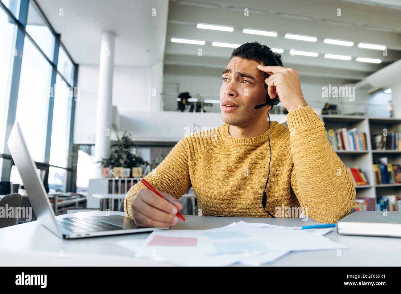 Müde hispanic Kerl, Freiberufler oder Student, arbeiten oder studieren aus der Ferne, macht Notizen, müde von Online-Unterricht oder Meetings Stockfoto