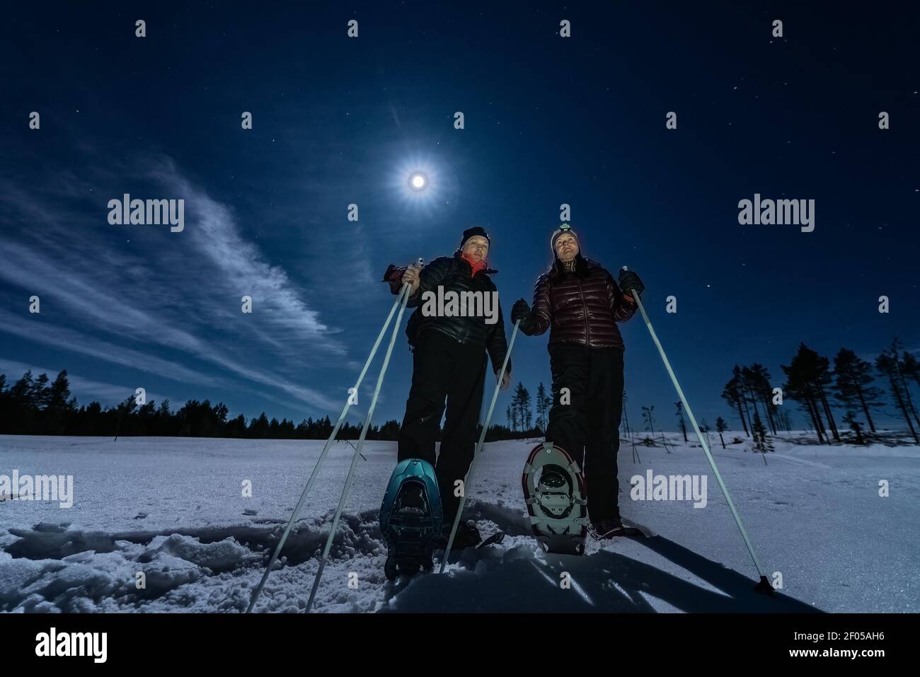 Schöne Männer und Frauen mittleren Alters in Schneeschuhen stehen in der Nacht selten verschneiten Winterwald unter Vollmondlicht. Nachtwanderung, Lappland, Umea, Schweden Stockfoto