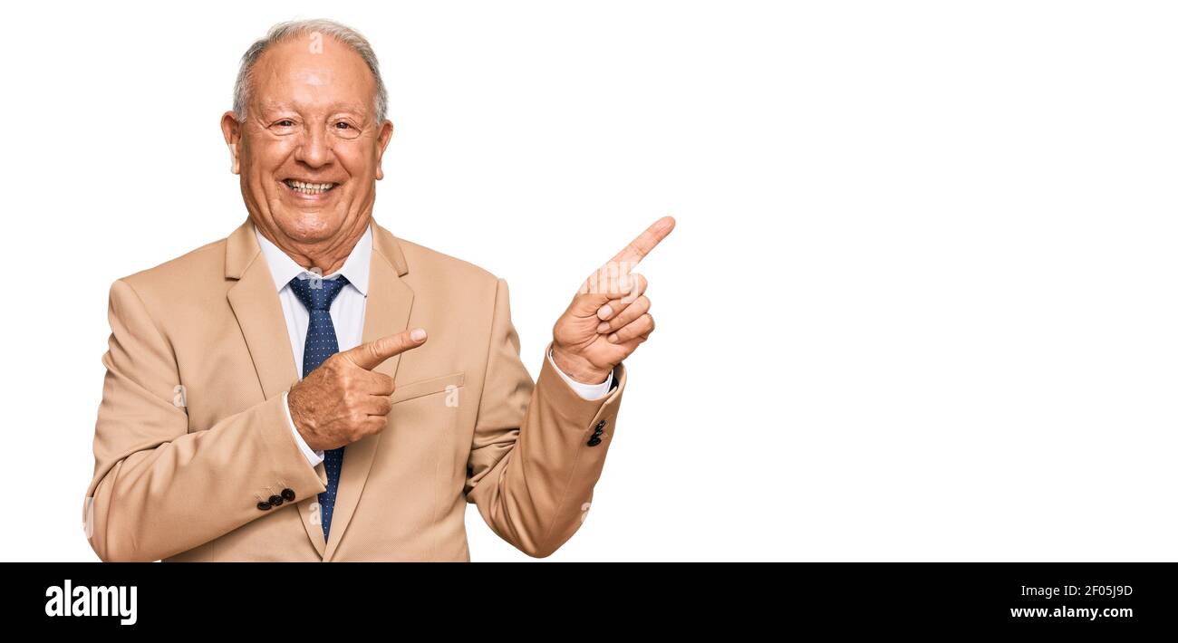 Leitender kaukasischer Mann in Business-Anzug und Krawatte lächelnd und Blick auf die Kamera mit zwei Händen und Fingern zur Seite zeigen. Stockfoto