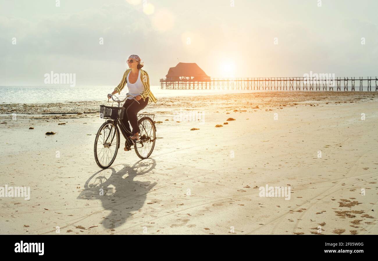 Frauen mittleren Alters gekleidet leichte Sommerkleidung Reiten alte Vintage Fahrrad Mit Vorderkorb auf der einsamen Ebbe Ozean weiß Sandküste auf Kiwengwa Stockfoto