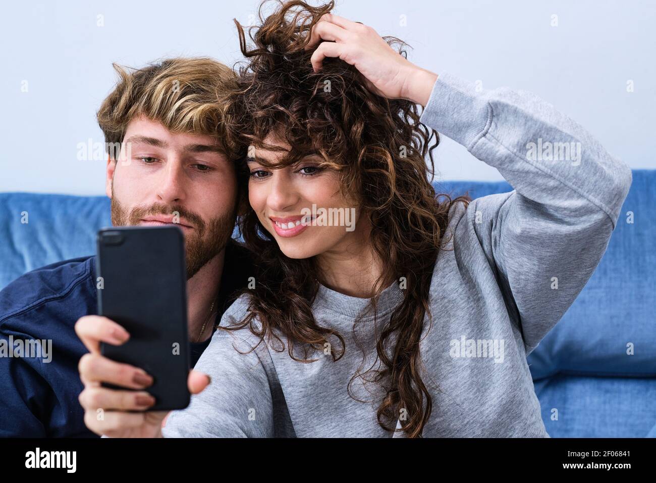 Junger bärtiger Mann, der einer lächelnden Frau in legerer Kleidung nahe kommt und Selfie auf dem Mobiltelefon nimmt Stockfoto