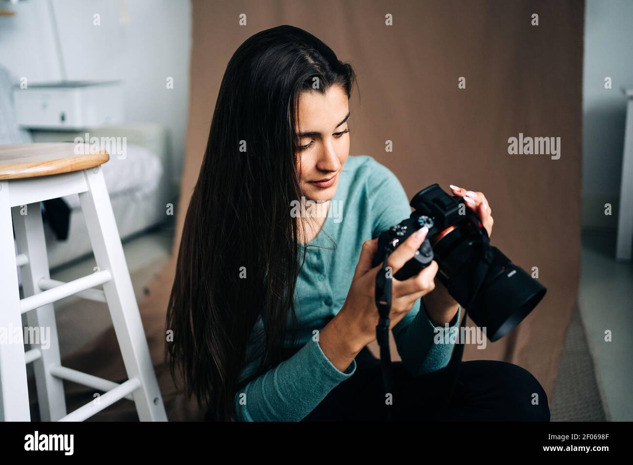 Millennial weiblich mit professioneller Fotokamera sitzt auf braun zerknittert Textiler Hintergrund zu Hause Stockfoto