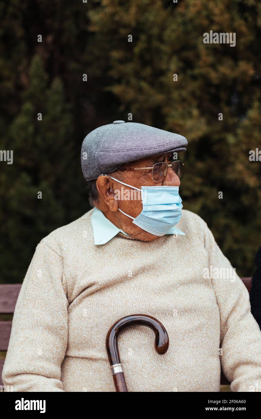 Porträt eines älteren Mannes mit Gesichtsmaske und Baskenmütze suchen Unterwegs auf einer Parkbank sitzen Stockfoto
