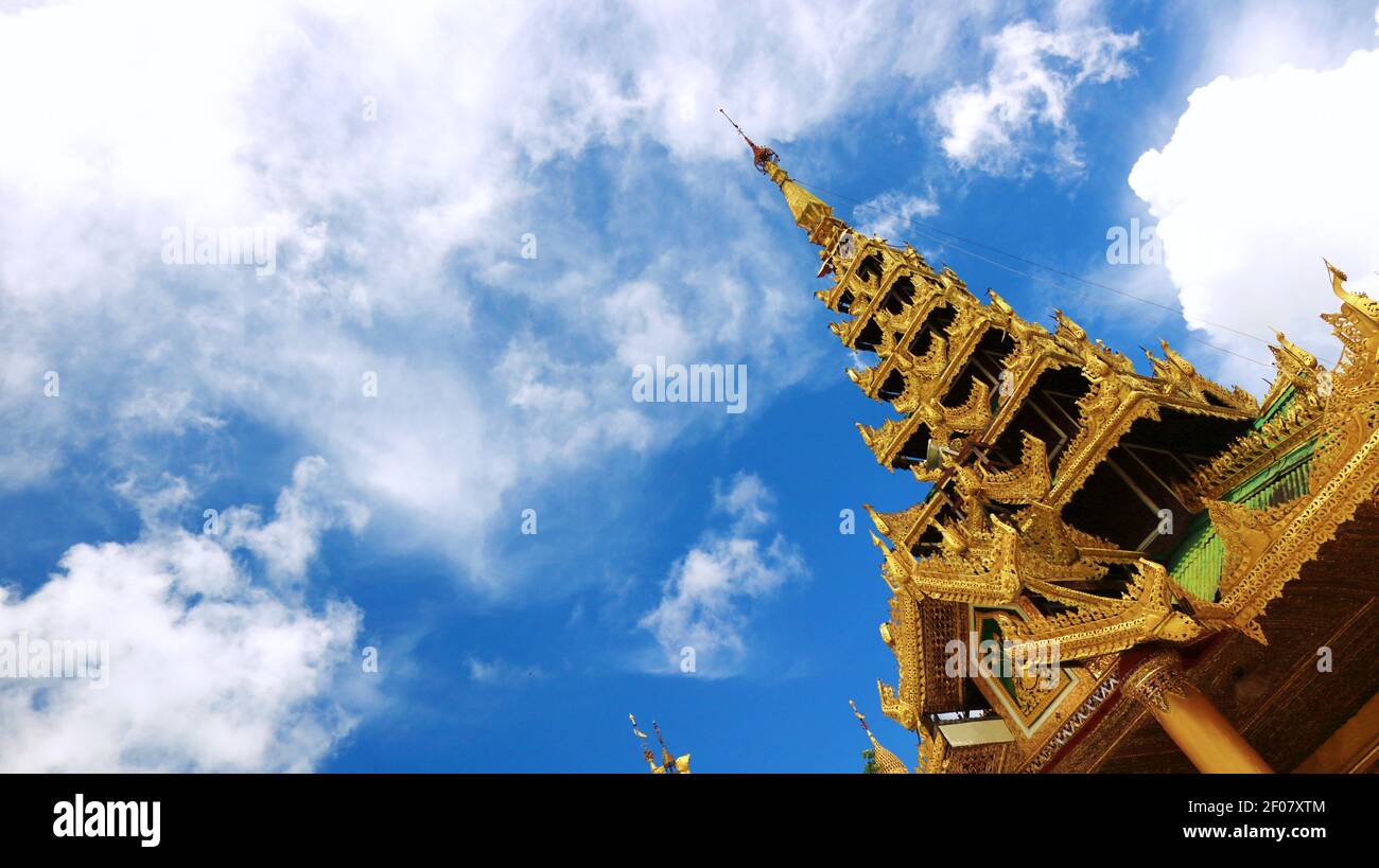 Gekippte Aufnahme eines goldenen Dachs eines kleinen Tempels und eines wolkigen und blauen Himmels im Shwedagon Pagoda Complex, Yangon, Myanmar (Burma) Stockfoto