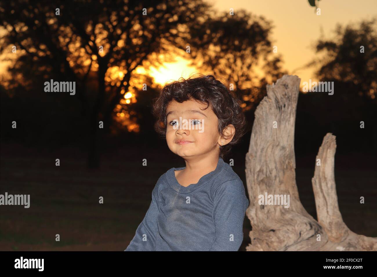 Ein indisches schönes lächelndes kleines Knabenkind, das im Feld draußen am Sonnenuntergang sitzt, indien. Konzept für lächelnde Kinder, Stolz des Landes heute childr Stockfoto