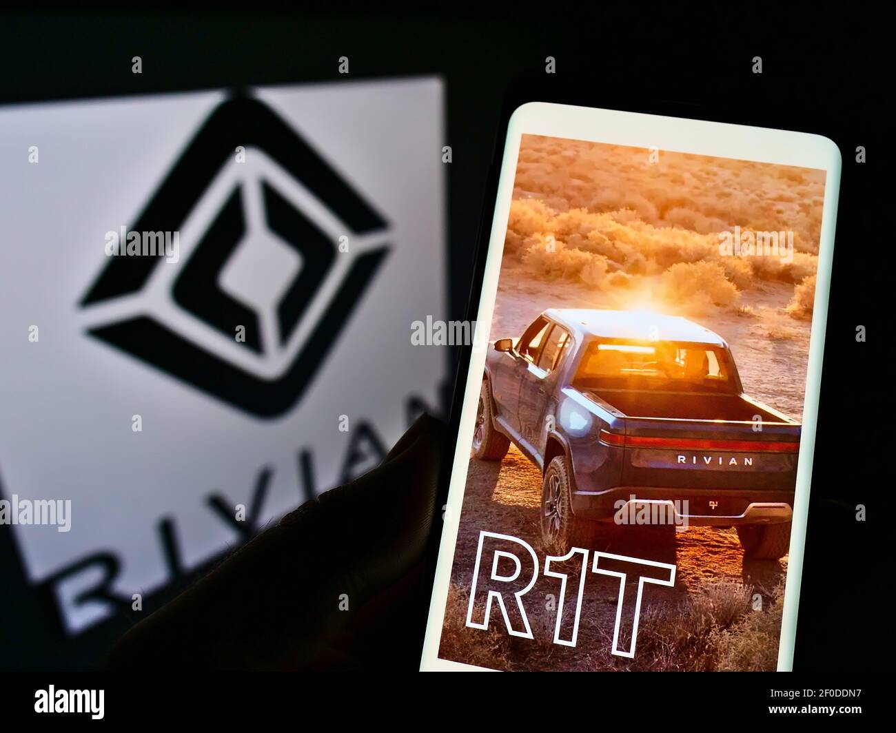 Person hält Handy mit Webseite der US-Elektrofahrzeug-Firma Rivian Automotive auf dem Bildschirm vor dem Logo. Fokus auf der Mitte des Telefondisplays. Stockfoto