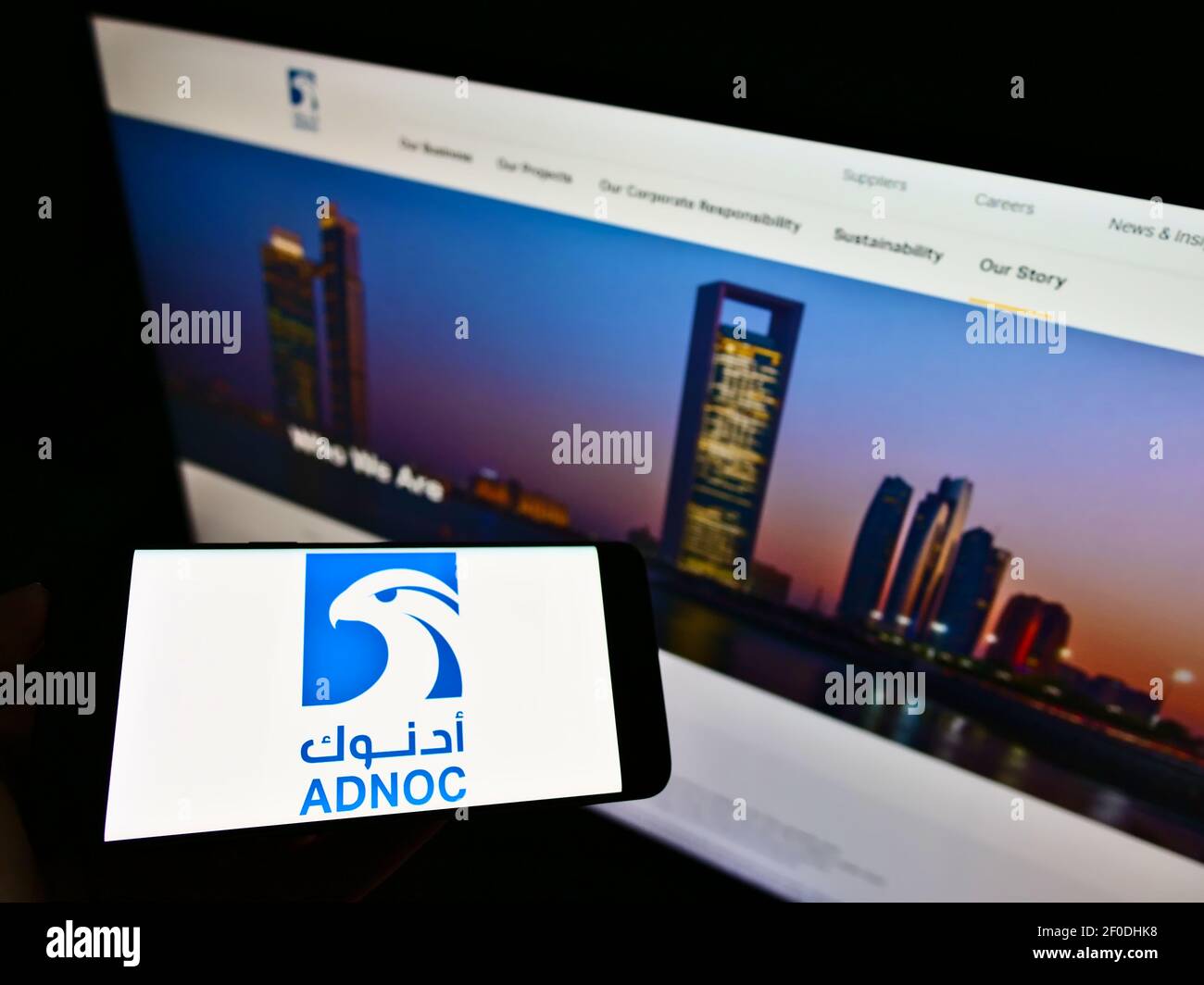 Person, die das Smartphone mit dem Logo der Abu Dhabi National Oil Company (ADNOC) auf dem Bildschirm vor der Website hält. Konzentrieren Sie sich auf die Telefonanzeige. Nicht modifiziertes Foto. Stockfoto
