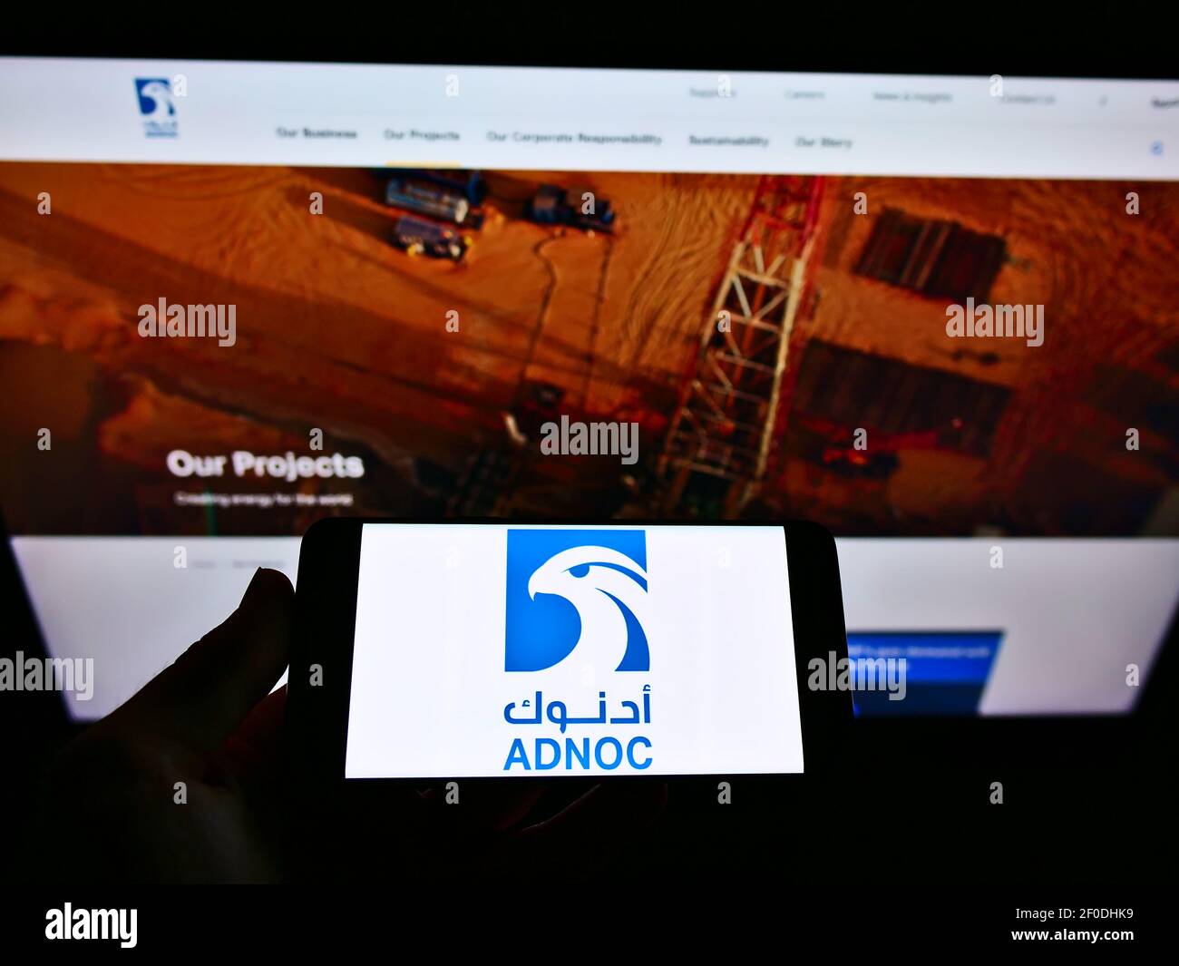 Person mit Mobiltelefon und Firmenlogo der Abu Dhabi National Oil Company (ADNOC) auf dem Bildschirm vor der Webseite. Fokus auf Handy-Display. Stockfoto