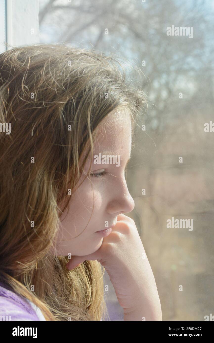 Das Mädchen im Teenageralter schaut morgens aus dem Fenster. Du kannst nicht gehen, es ist traurig. Nahaufnahme, Seitenansicht. Stockfoto
