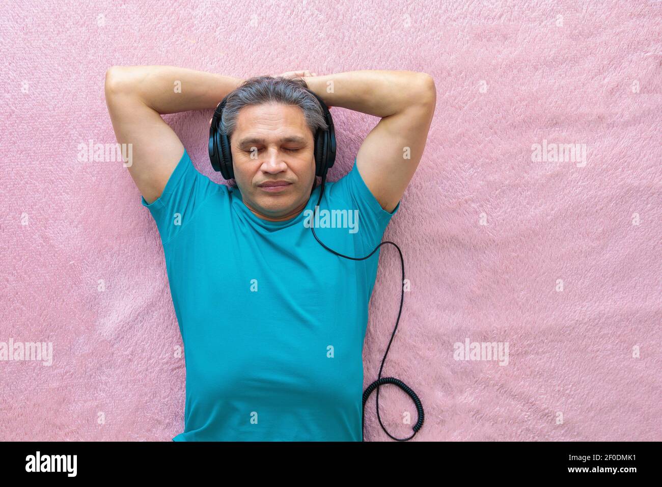 Der 50-jährige Mann hört Musik mit Kopfhörern zu Hause, auf dem Bett liegend. Entspannend, genießend. Stockfoto