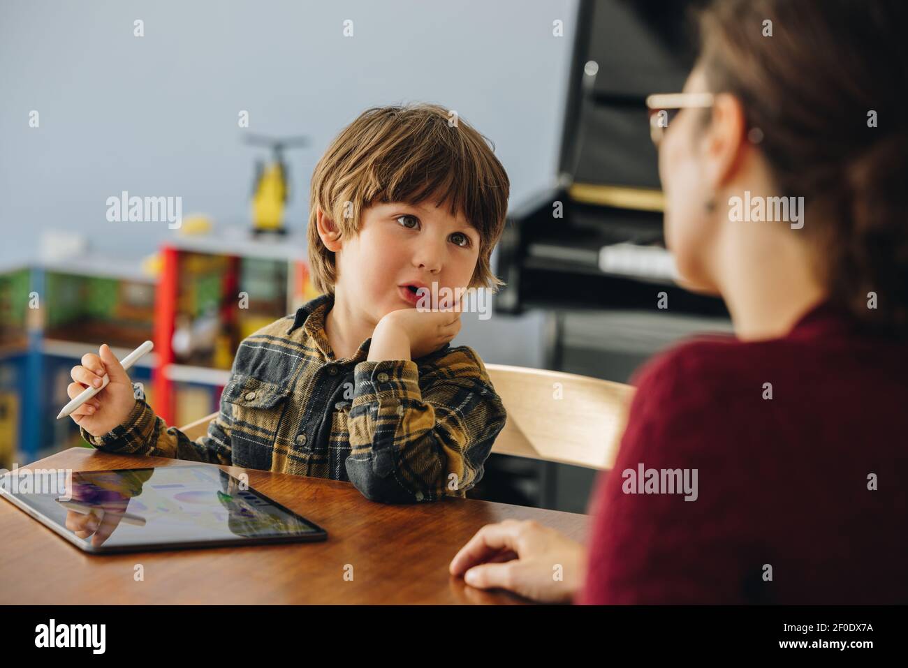 Netter Junge im Gespräch mit Mama, während mit digitalen Tablet. Sohn, der zu Hause mit seiner Mutter spricht. Stockfoto