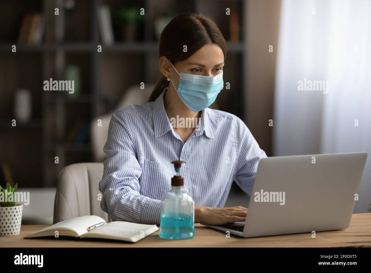 Weibliche Mitarbeiterin in Gesichtsmaske Arbeit auf Laptop online Stockfoto