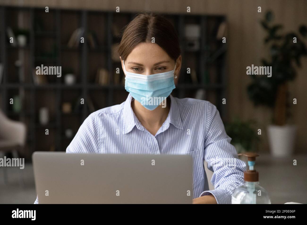 Kaukasische Mitarbeiterin im Facemask arbeiten auf Laptop Stockfoto