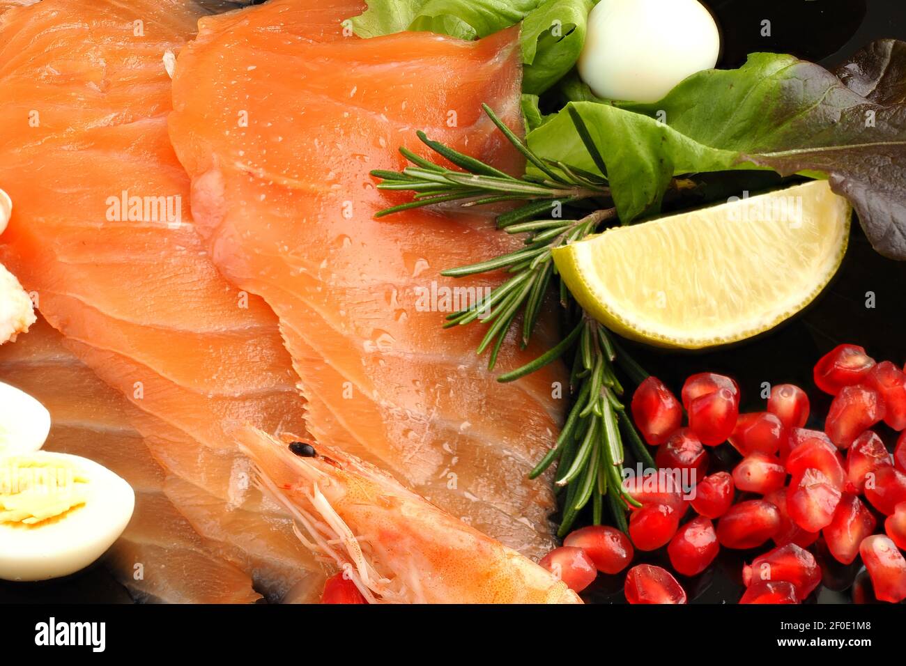 Roter Fisch. Scheiben gesalzener Lachs auf einem Teller mit Zitronengrün und Granatapfelkörnern. Stockfoto