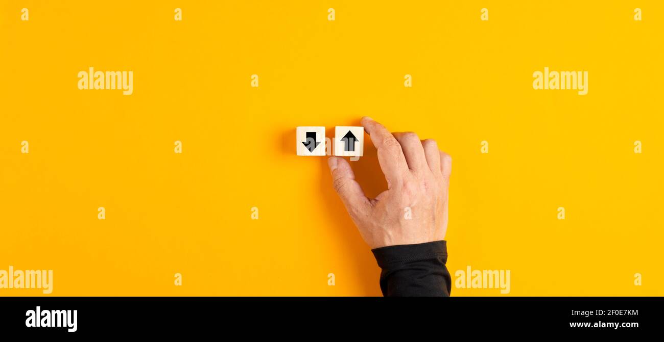 Holzwürfel mit Pfeil nach oben und unten mit einer männlichen Hand Wahl der Pfeil nach oben auf gelbem Hintergrund. Stockfoto