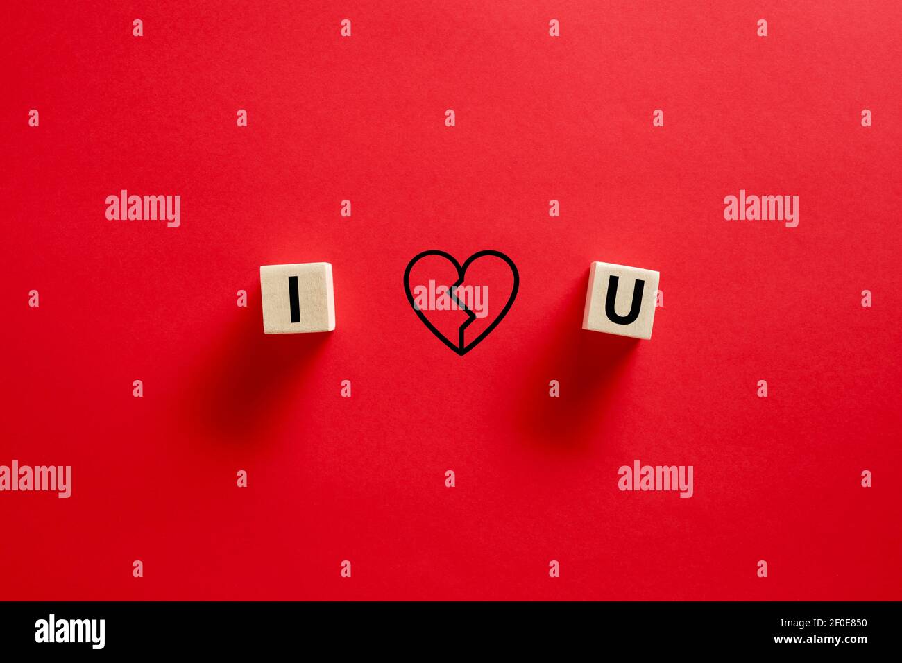 Ich liebe dich Wort geschrieben auf Holzwürfel mit einer Hand gezeichnet gebrochenen Herzform vor rotem Hintergrund. Trennung, Scheidung oder Trennung Konzept. Stockfoto