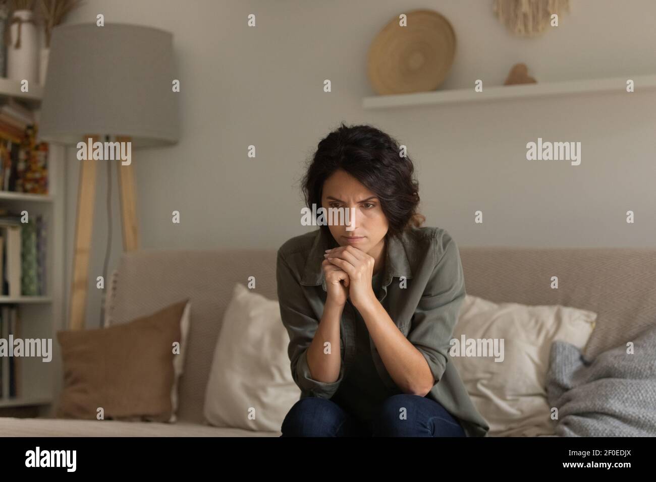 Nachdenkliche nervöse Frau sitzen auf dem Sofa versuchen, Emotionen zu kontrollieren Stockfoto