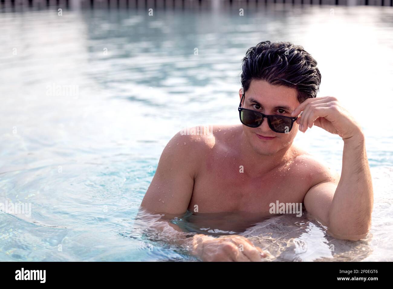 Porträt eines attraktiven jungen Mannes in Sonnenbrille auf Kante ruhen Des Swimmingpools Stockfoto