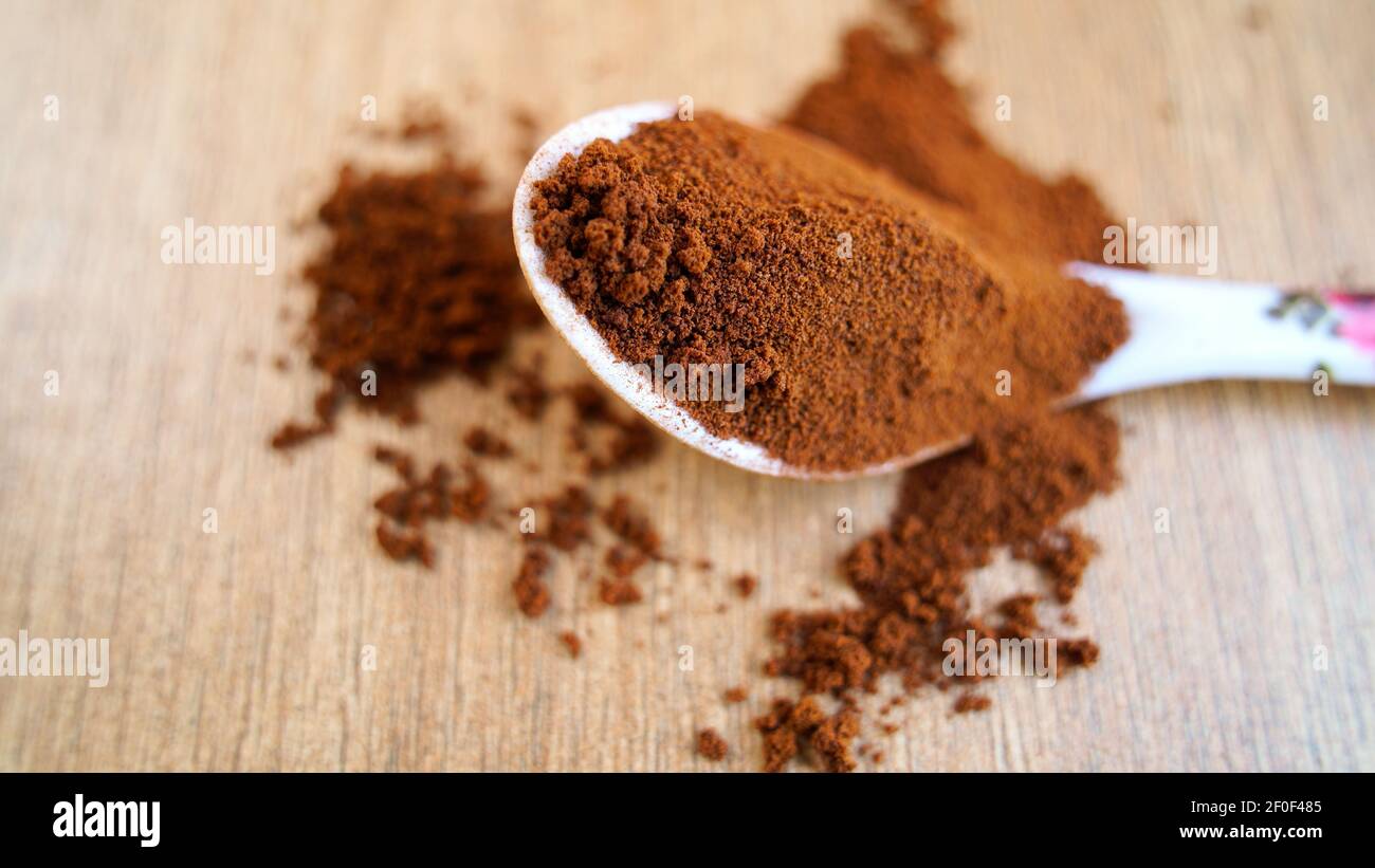 Kaffeepulver im Löffel isoliert auf Tisch Holzhintergrund. Stapel von braunem Kaffee, der auf dem Boden verschüttet wird, Ansicht von oben, indische Gewürze Stockfoto