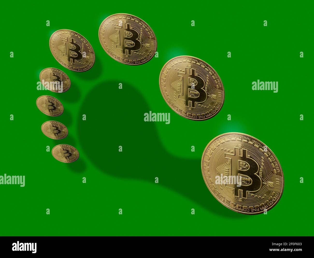 Bitcoin-Token angeordnet, um den Schatten eines Fußabdrucks zu bilden Auf einem grünen Hintergrund Stockfoto