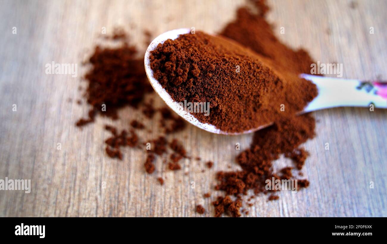 Kaffeepulver im Löffel isoliert auf Tisch Holzhintergrund. Stapel von braunem Kaffee, der auf dem Boden verschüttet wird, Ansicht von oben, indische Gewürze Stockfoto