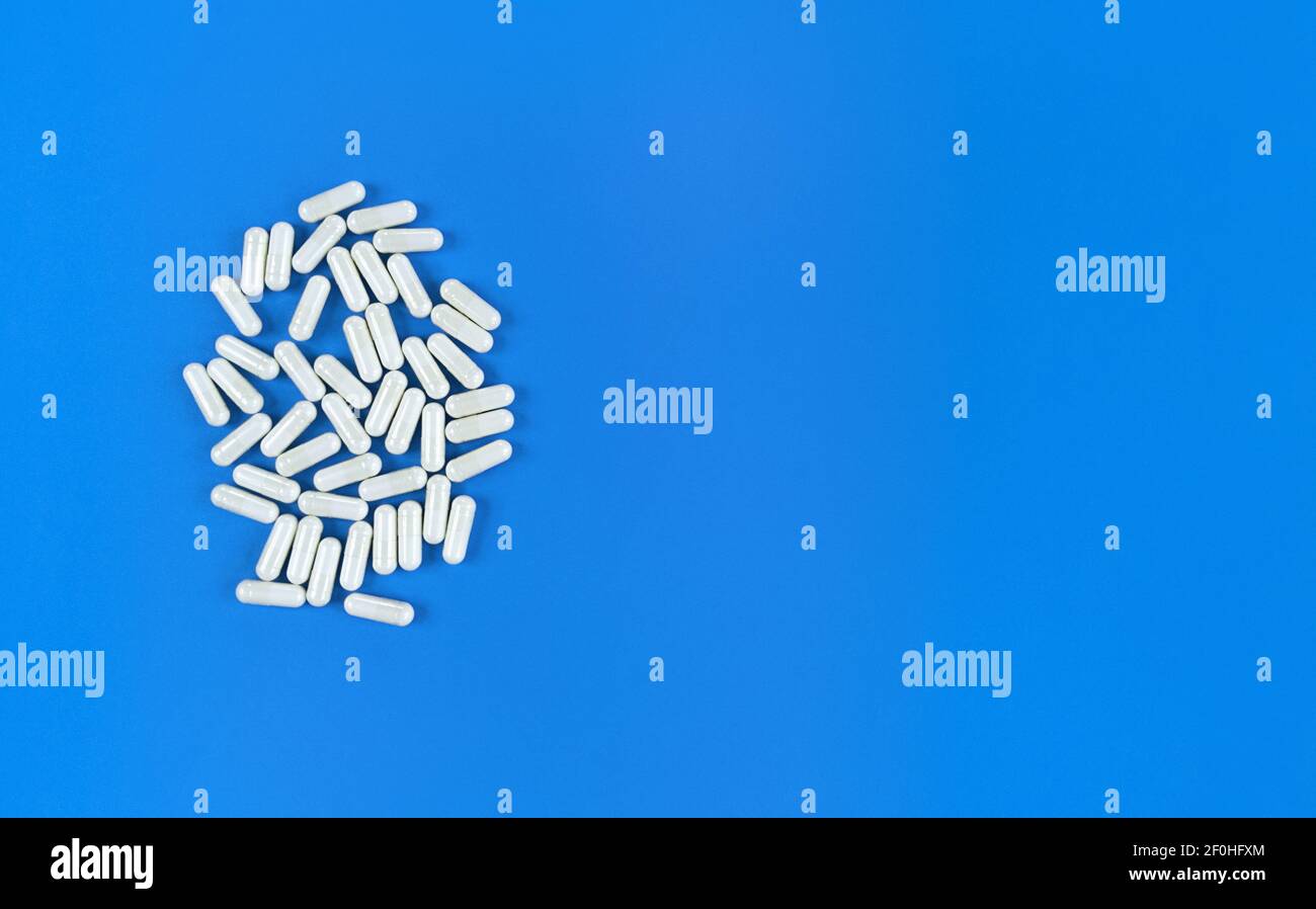 Weiß verstreute Pillen Kapseln auf blauem Hintergrund mit Kopierraum. Stockfoto