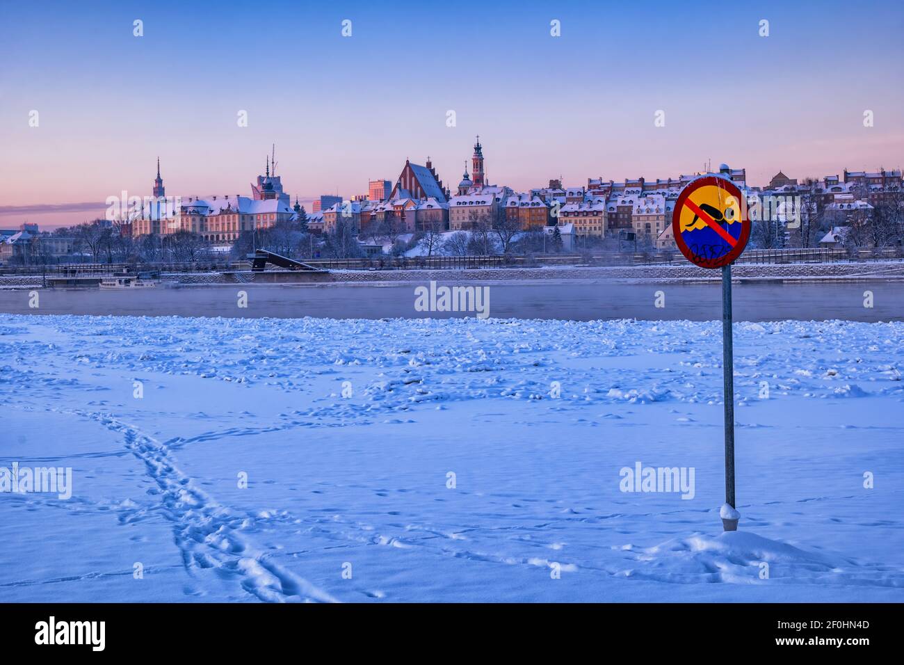 Kein Schwimmwarnschild am verschneiten Strand am Fluss Wisla im Winter, Stadt Warschau bei Sonnenaufgang in Polen, Altstadt Skyline im Hintergrund. Stockfoto