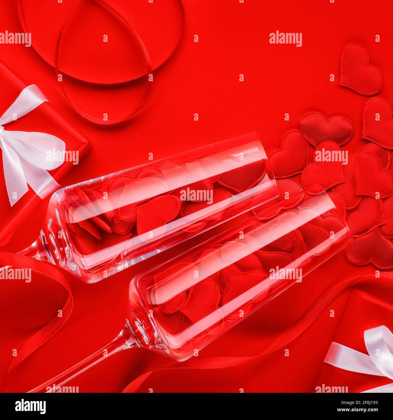 Zwei Glas elegante Champagner Gläser auf einem leuchtend roten Hintergrund mit Satin Herzen und Geschenke mit weißen Schleifen. Nahaufnahme, Draufsicht. Stockfoto