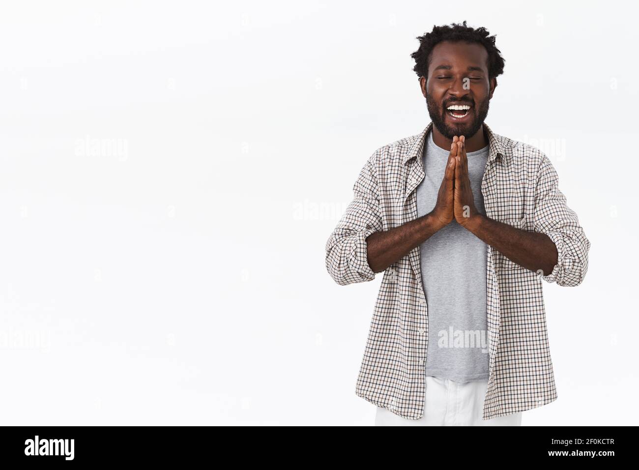 Entspannter und friedlicher fröhlicher afroamerikanischer bärtiger Mann mit Afro-Frisur, Wunsch machend oder Namaste sagend, mit zusammengeklemmten Händen betend Stockfoto