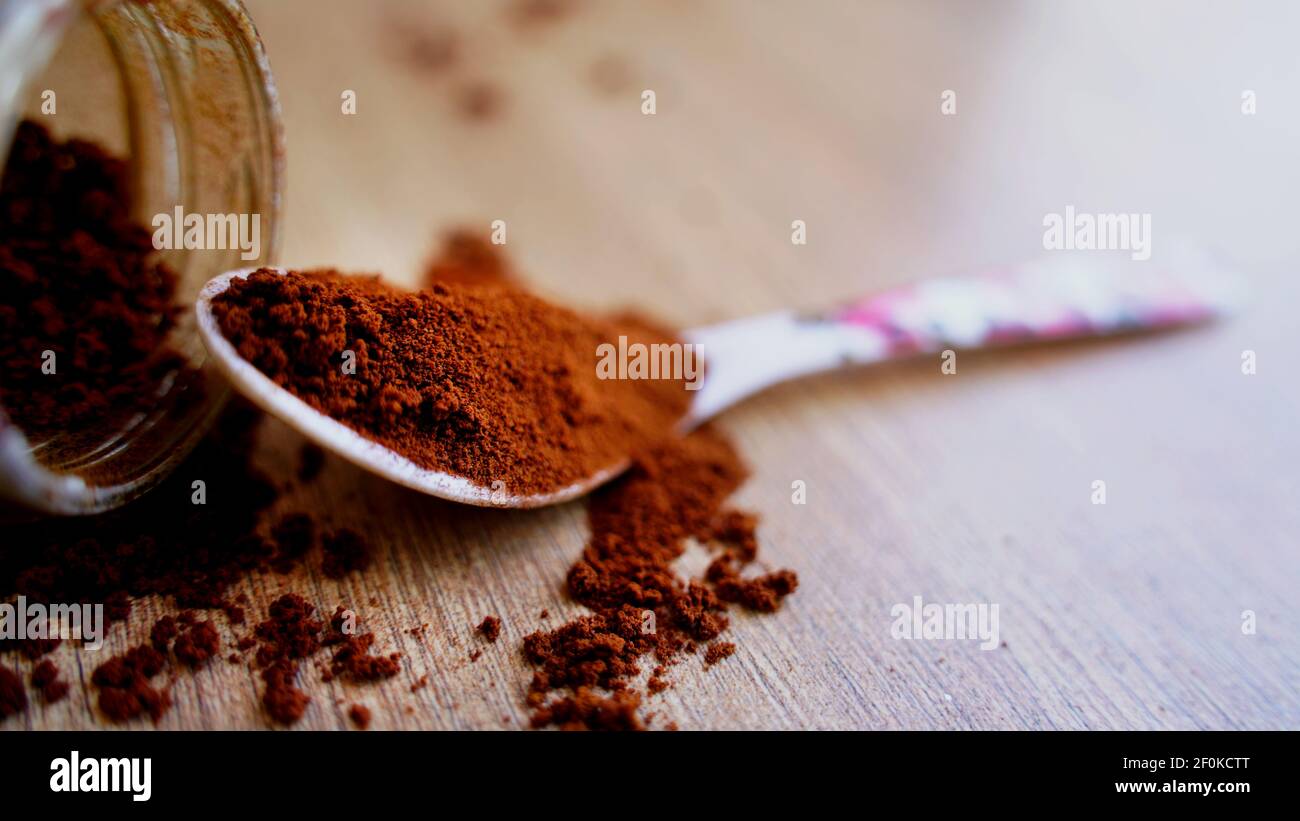 Kaffeepulver verschüttet auf dem Holztisch mit weißem Löffel. Stapel von braunem Kaffee mit einem Glas in unscharfen Hintergrund. Makroansicht von oben, Indien Stockfoto