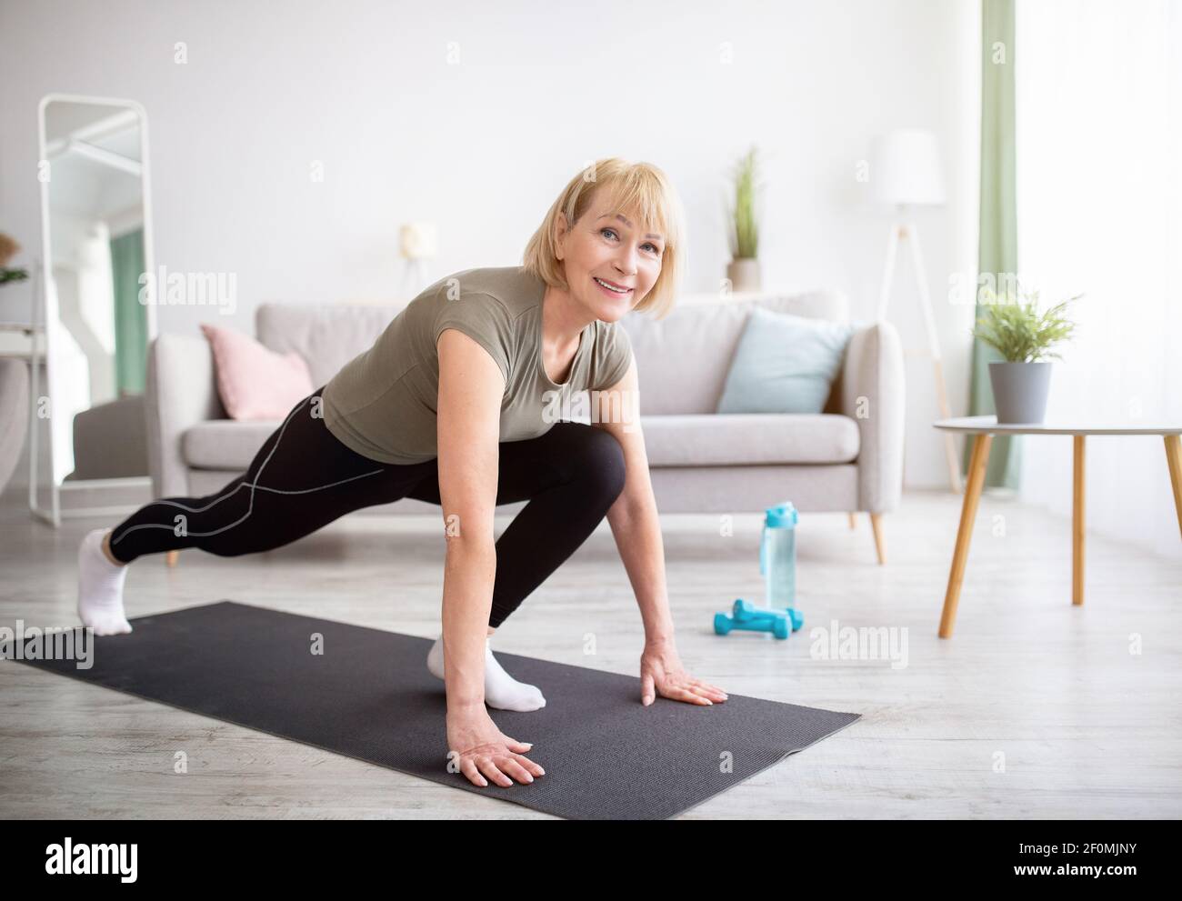 Positive sportliche ältere Frau beim Joga-Ausfallschritt beim Heimtraining, Platz kopieren Stockfoto