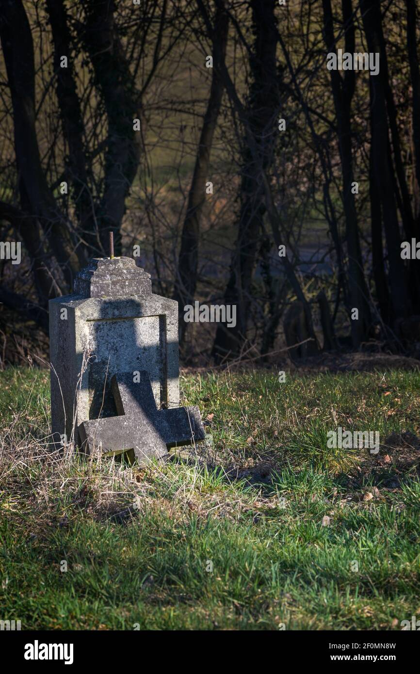 Alte Grabsteine mit gebrochenem Kreuz, aber mit einem Schatten in Kreuzform unter Bäumen auf einem verlassenen Friedhof, religiöses Symbol, Kopierraum, ausgewählter Fokus Stockfoto