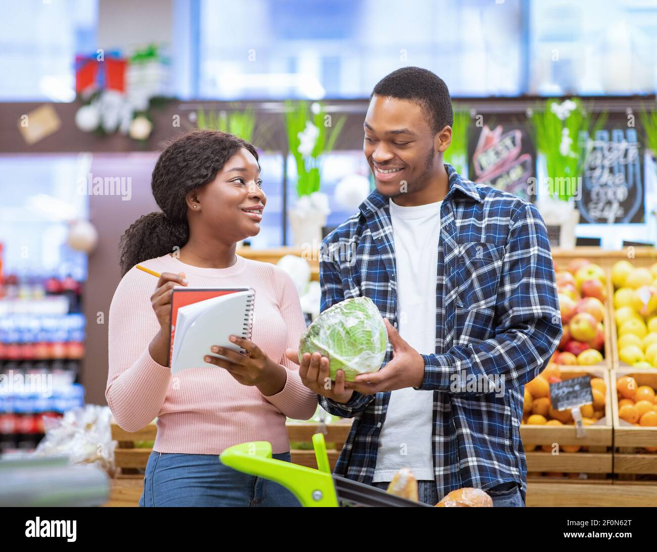 Einkaufen während des Coronavirus-Ausbruchs. Millennial schwarzes Paar Kauf frisches Gemüse, Überprüfung der Lebensmittelliste im Einkaufszentrum Stockfoto