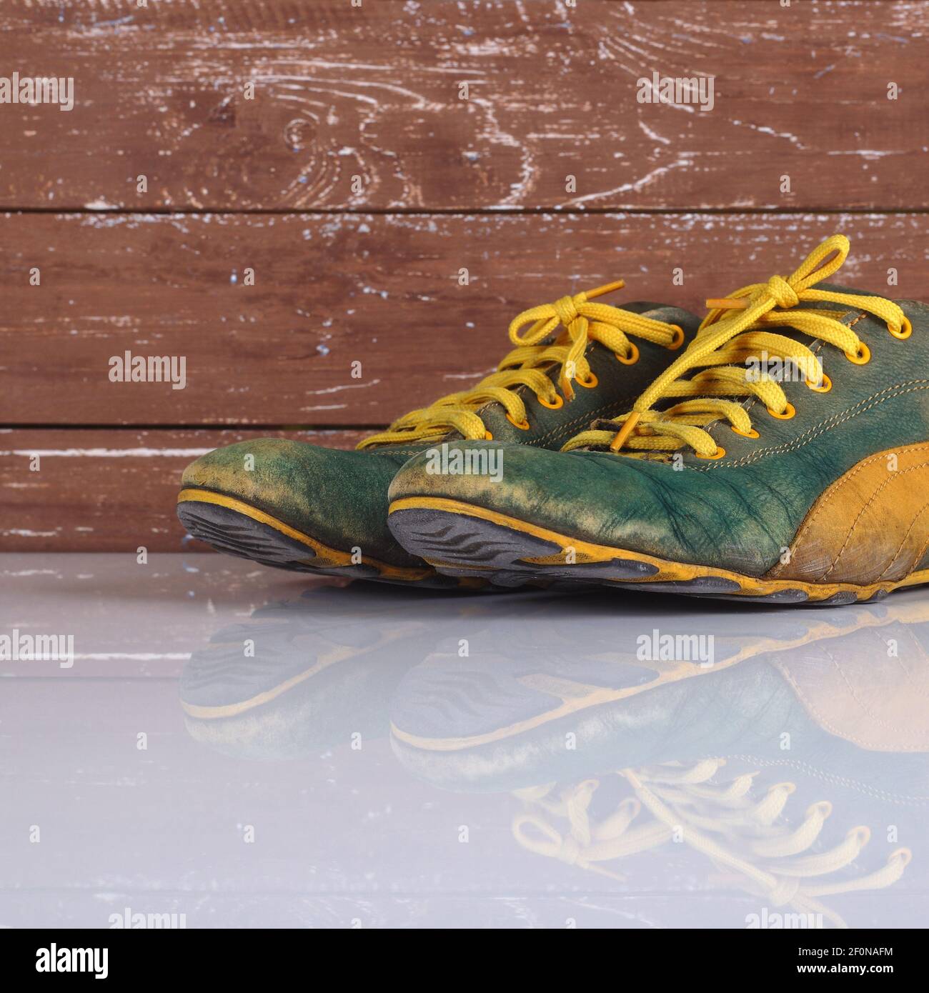 Kleidung Schuhe und Accessoires - Closeup alte Paar grün und Gelbe Turnschuhe Holzhintergrund mit Reflexion Stockfoto