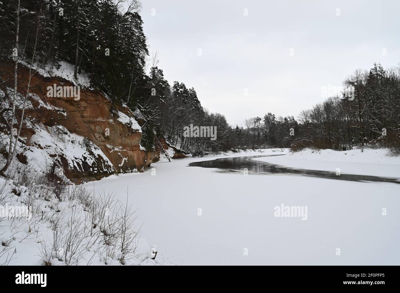 Blick auf die fast vollständig gefrorene Flussbiegung im Winter an den beeindruckenden orange-braunen Klippen. Stockfoto