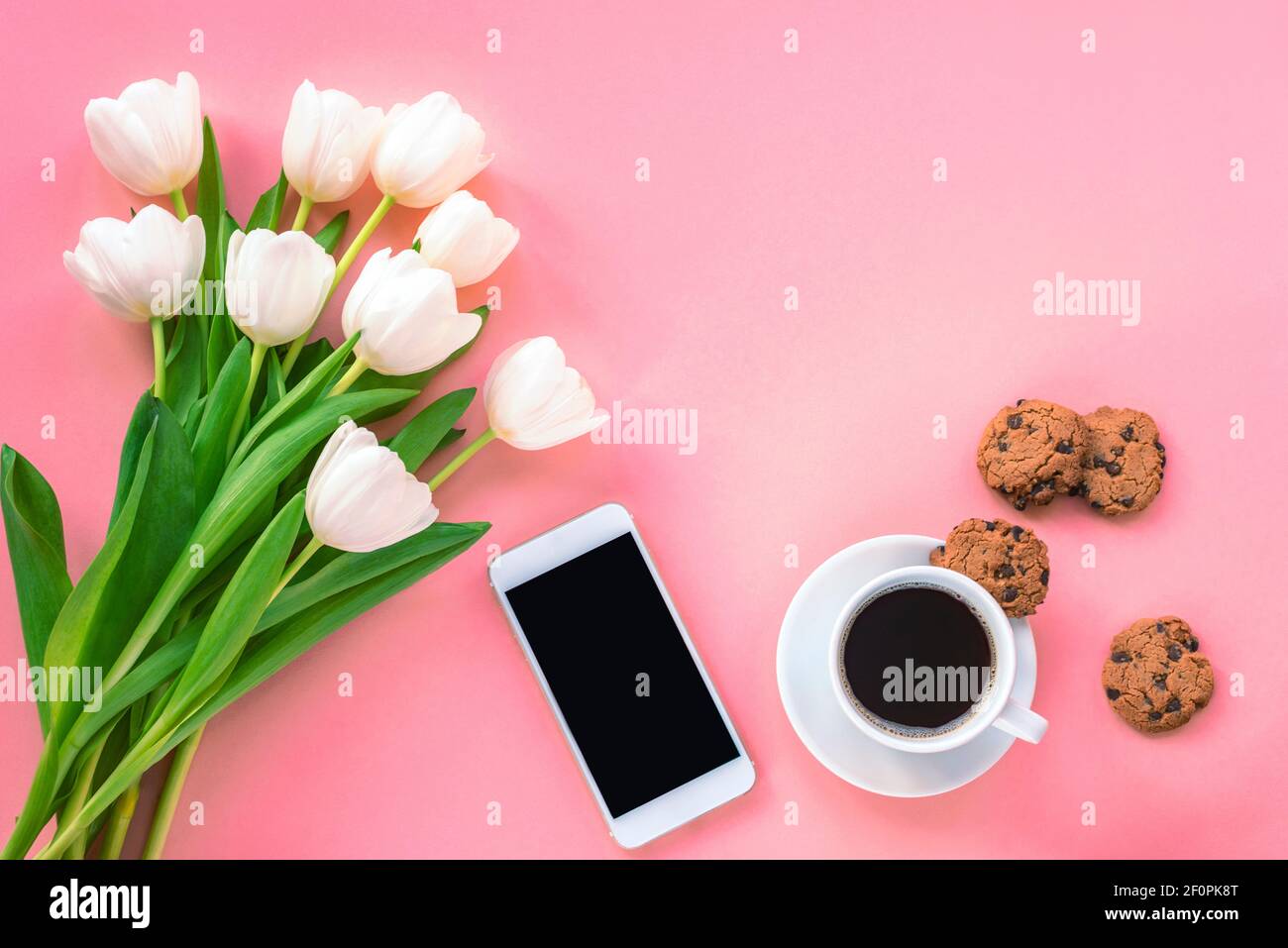 Tasse Kaffee, Chocolate Chip Cookies, Smartphone und weiße Tulpen auf rosa Hintergrund, Draufsicht. Frauentag oder Muttertag Konzept. Flach liegend, Kopie s Stockfoto