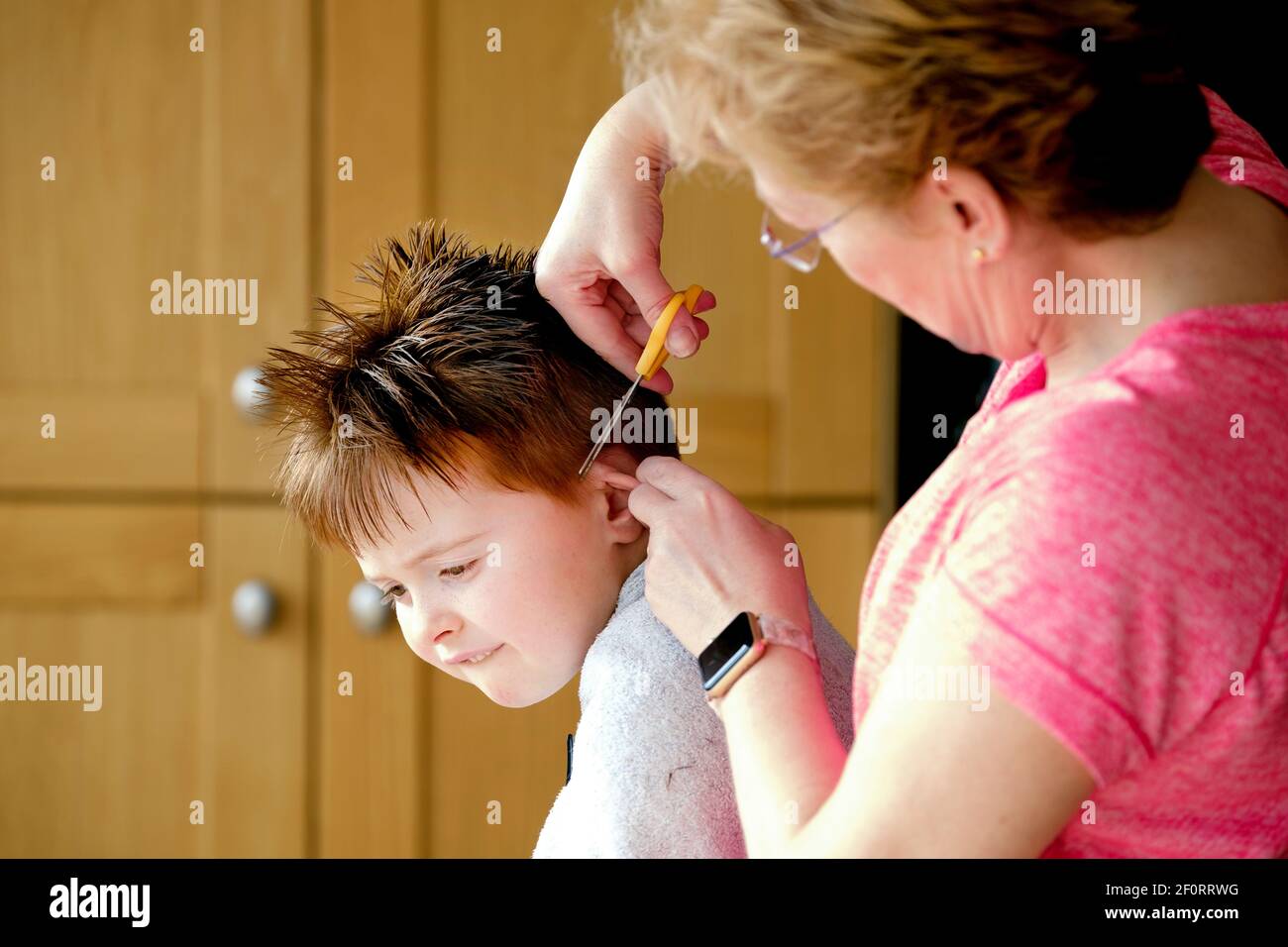 Ein kleiner Junge bekommt von seiner Großmutter einen Haushaarschnitt. Mit Friseure noch während der Sperre geschlossen Familien haben auf YouTube Selbsthilfe-Video zurückgegriffen Stockfoto